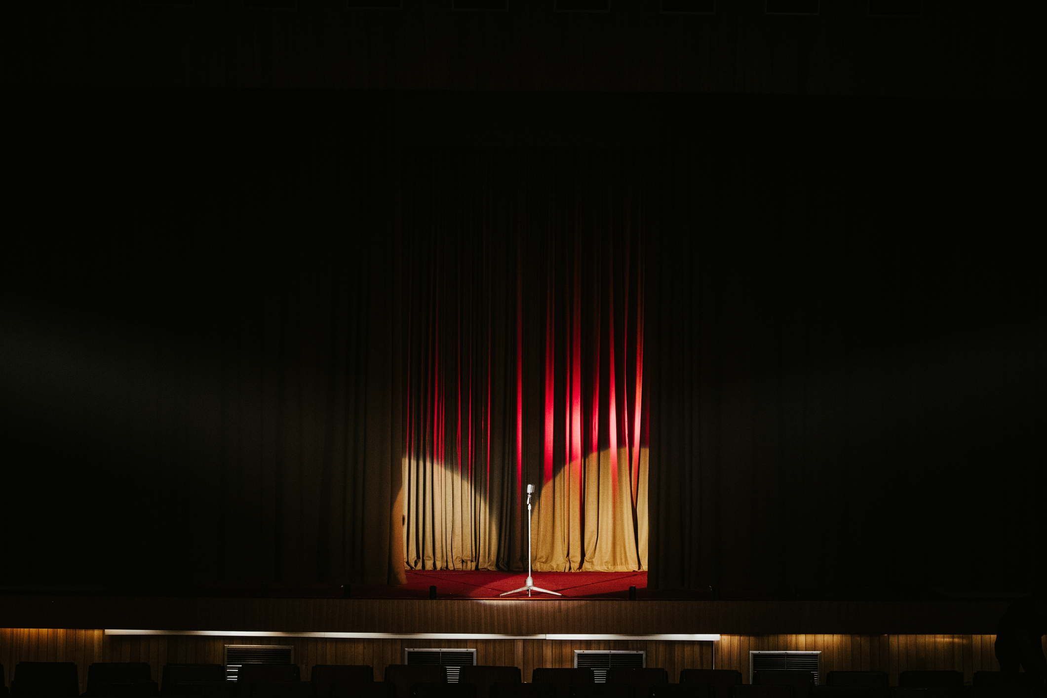 Image of an empty stage with closed curtain, microphone, and spotlight
