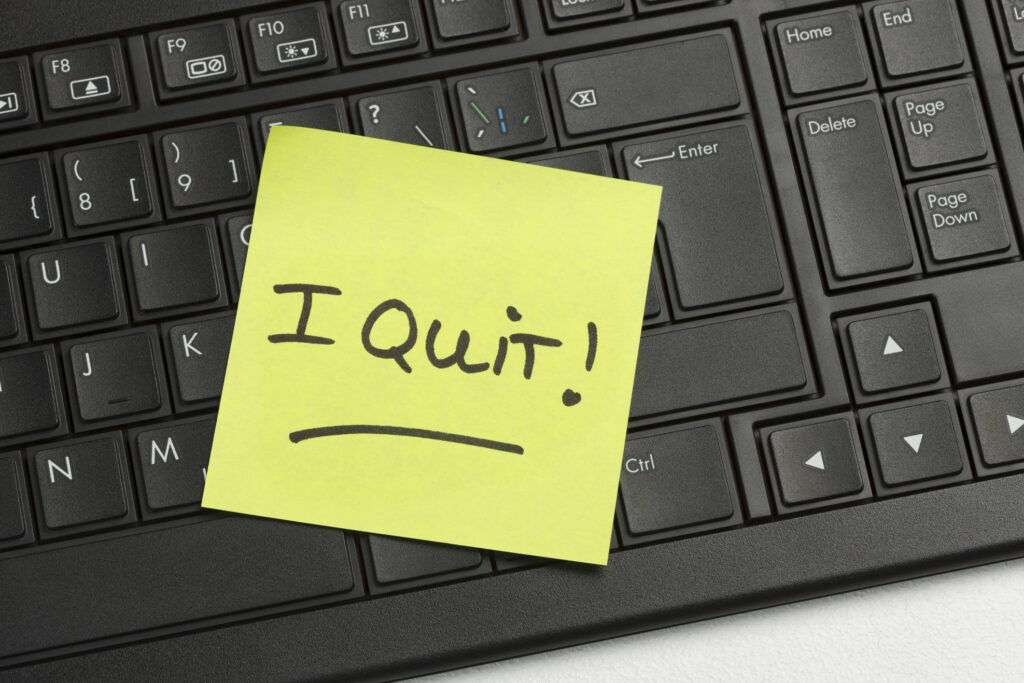 Image of a post-it note that reads "I quite" affixed to a computer keyboard